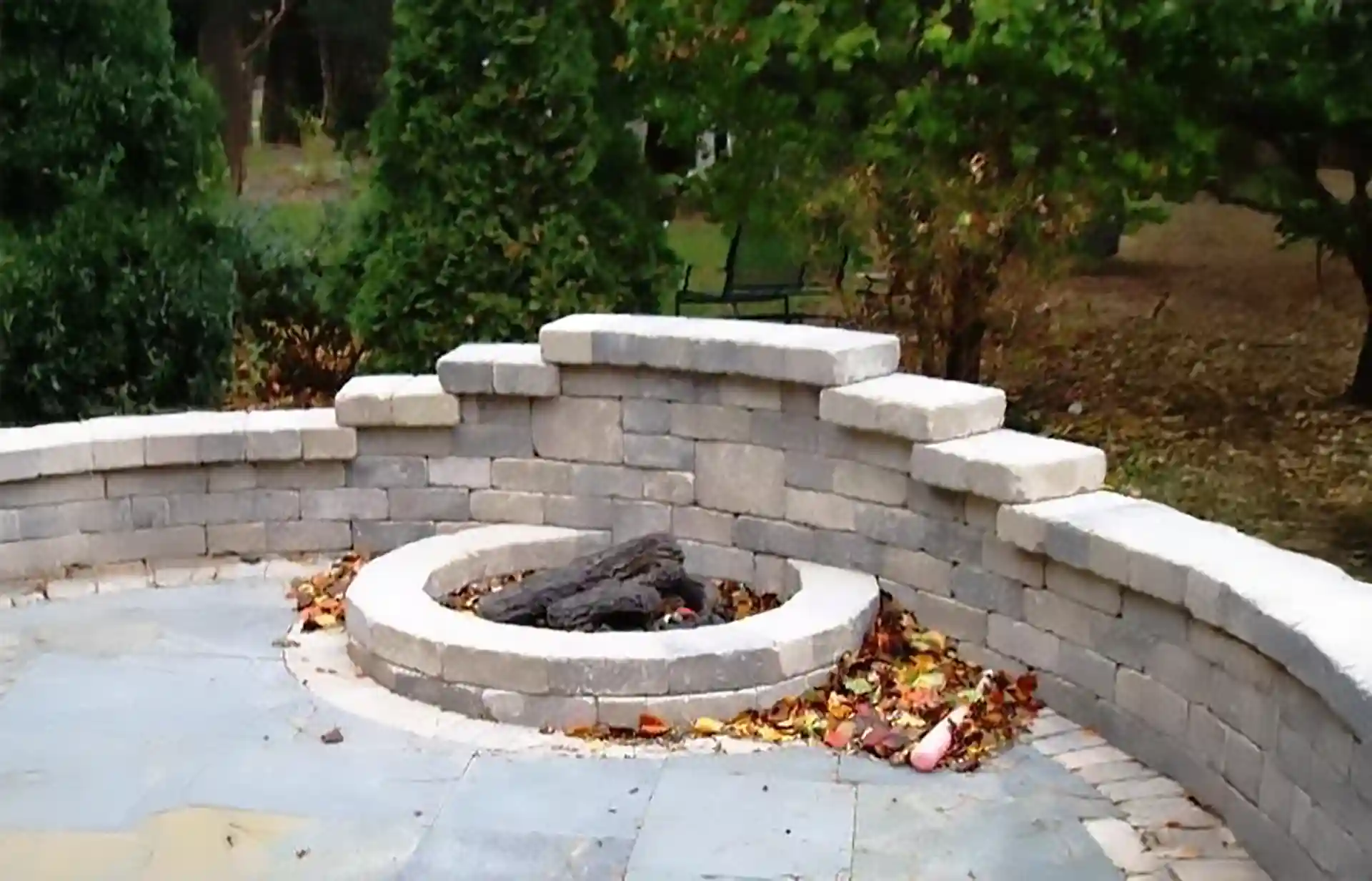 Stone firepit with a curved retaining wall on a patio.
