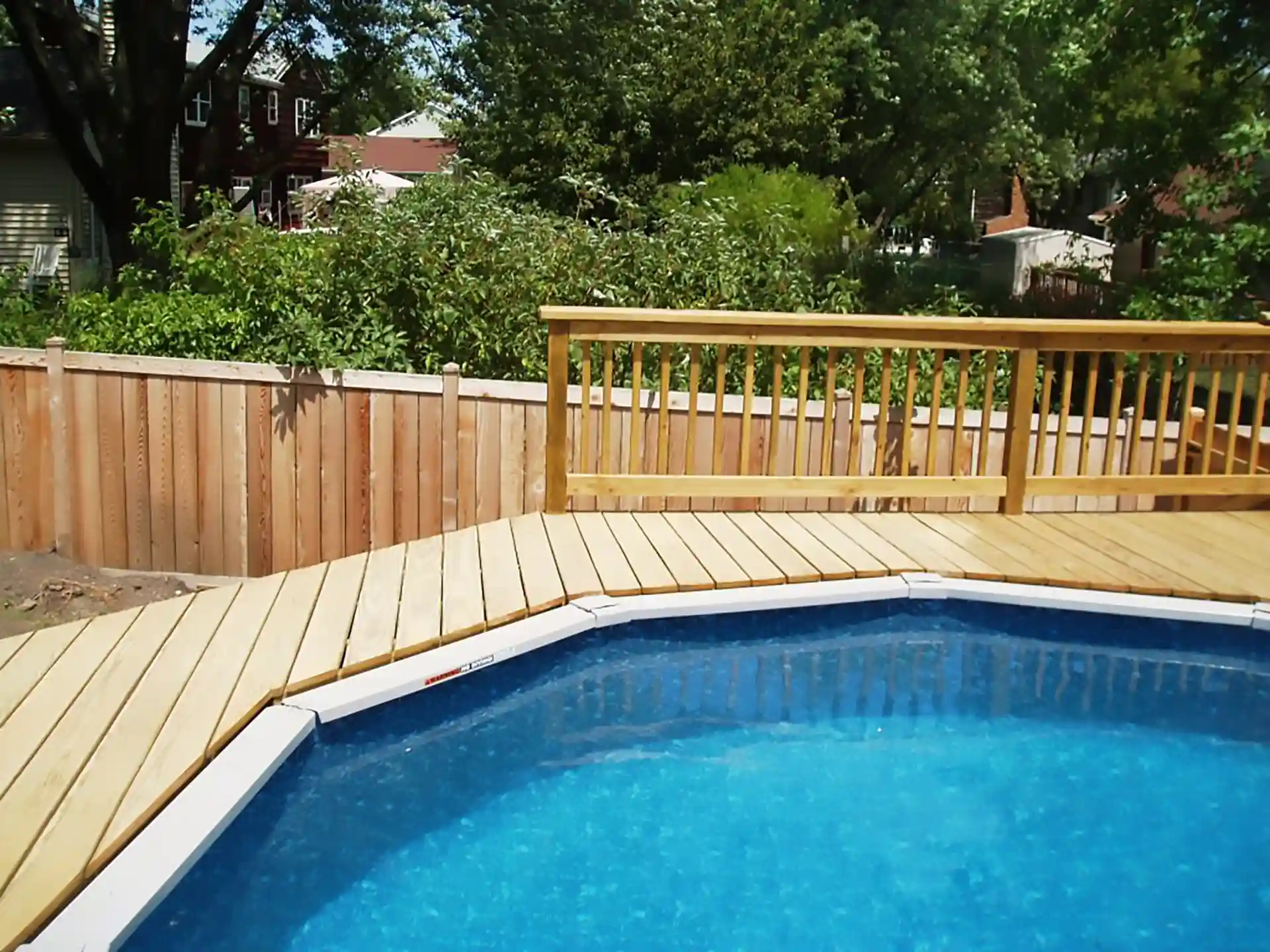 Photo of fresh wood deck built around blue above-ground pool and wooden privacy fence.