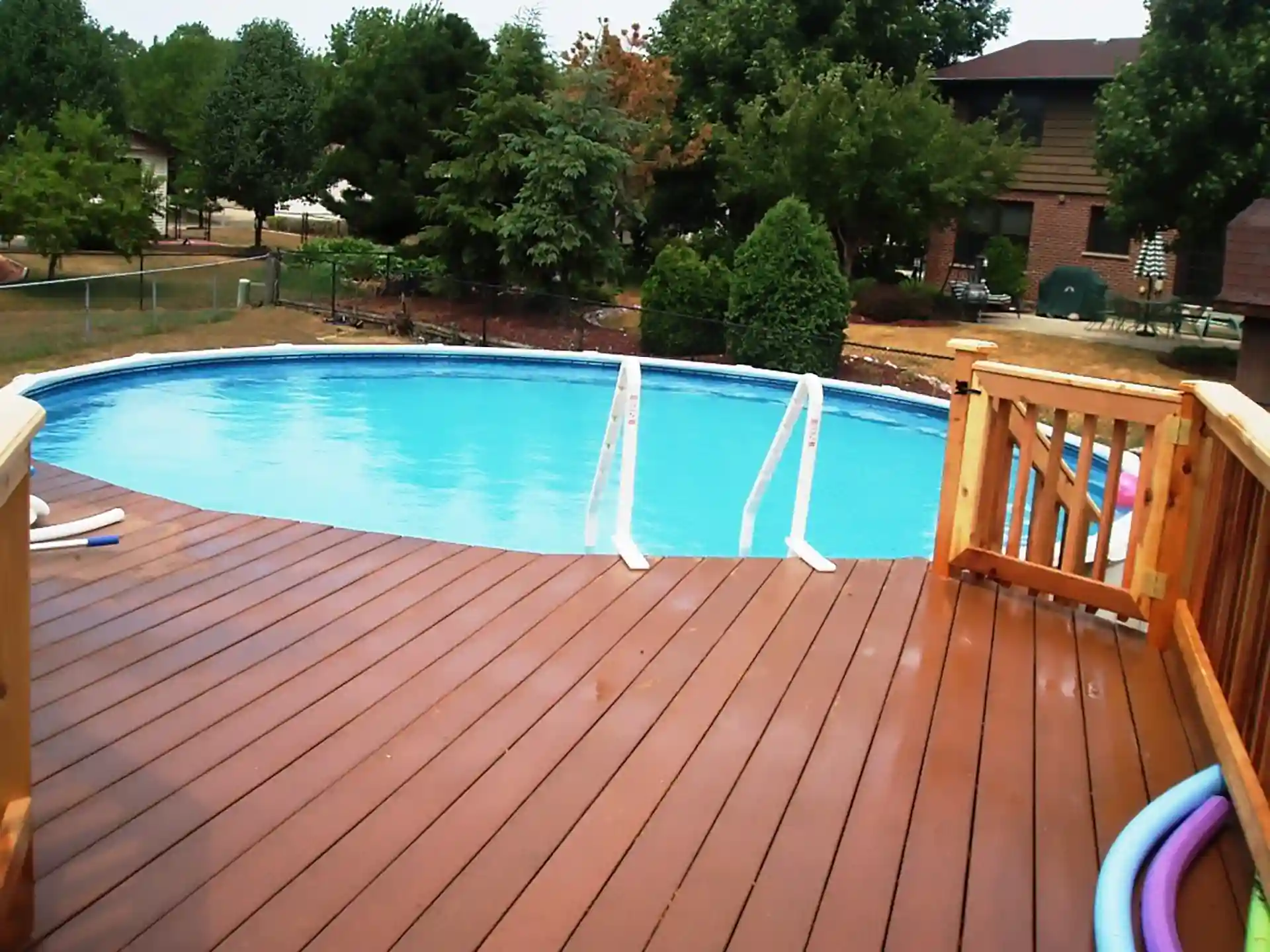 Photo of reddish-brown composite pool deck with wood gate and white pool ladder.