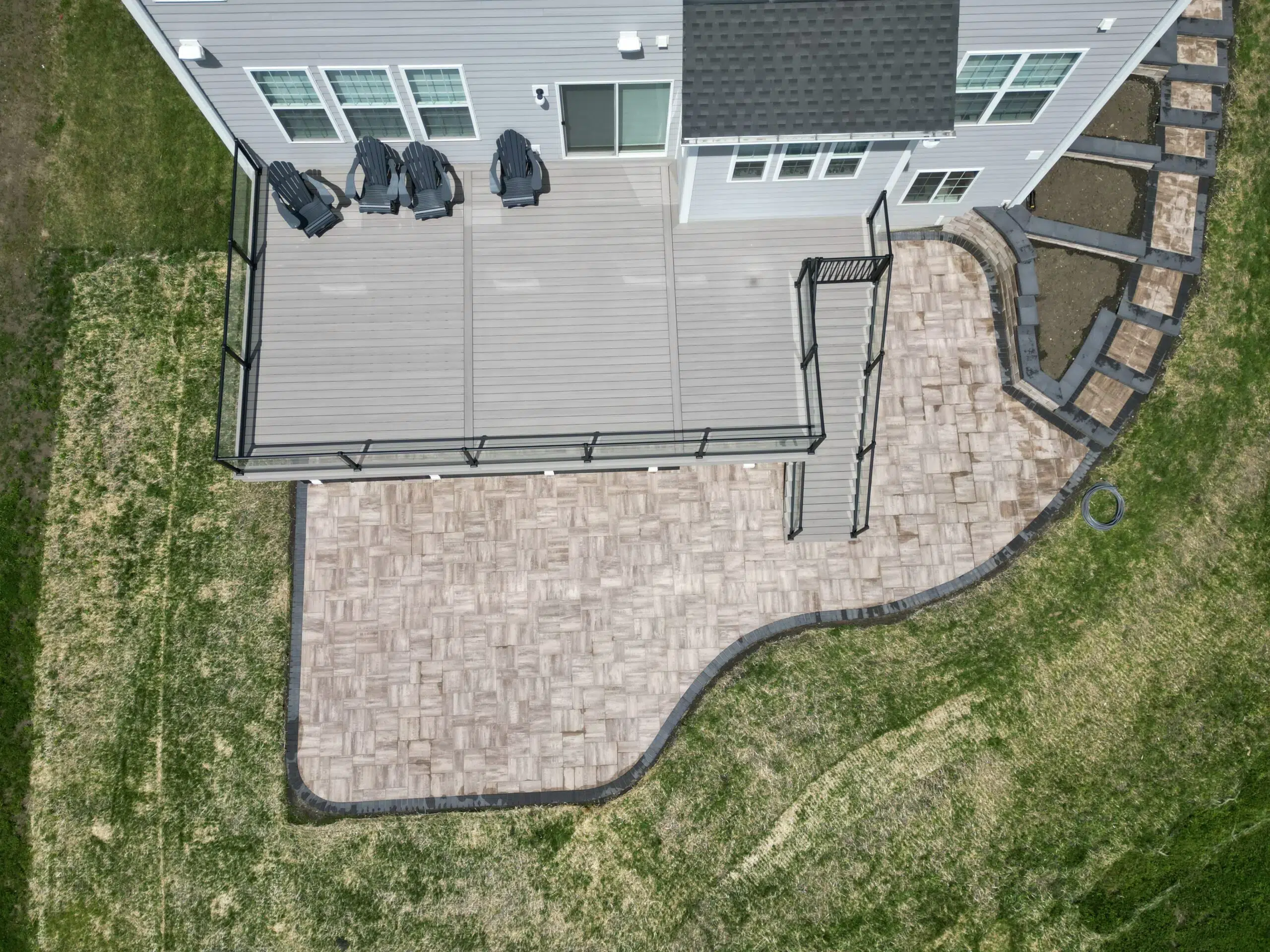 Aerial view of a custom deck that is elevated with deck steps, a gate, patio below, and hardscaping
